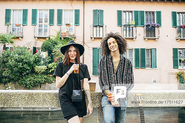 Lächelndes Paar hält Getränke in der Hand und steht vor einem Gebäude in der Stadt