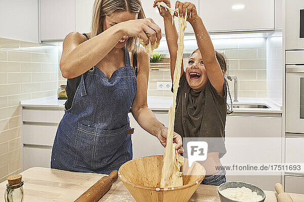 Mother with playful daughter kneading pizza dough in kitchen at home