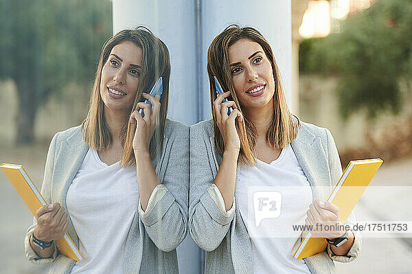 Reflection of businesswoman on window glass while talking on mobile phone