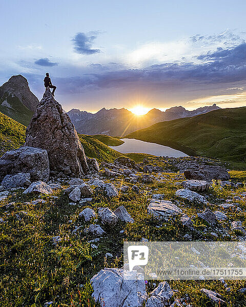 Wanderer sitzt auf einem Felsen bei Sonnenuntergang am Rappensee  Bayern  Deutschland