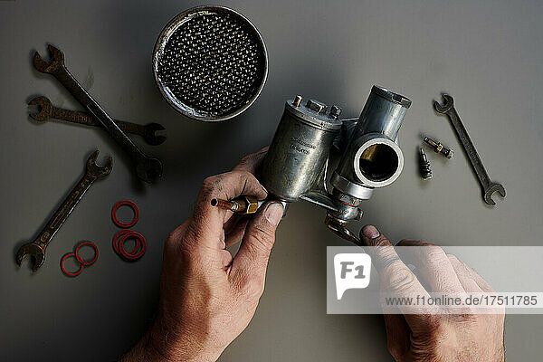 Top view of hand with vintage carburetor and tools in front of grey background