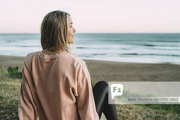 Young woman looking at sea while sitting on beach during sunset