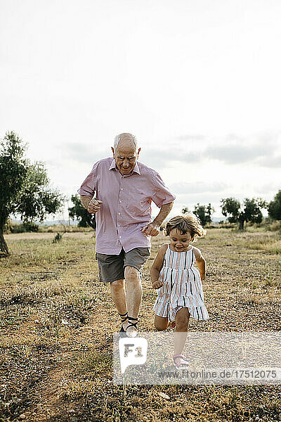 Verspielter Großvater und Enkelin laufen an Land gegen den Himmel