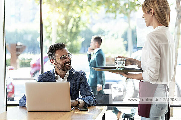 Smiling businessman looking at waitress holding glass of water in restaurant