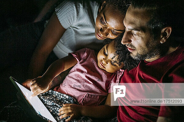 Parents with daughter using digital tablet while relaxing on bed at home