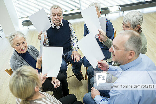 Group of seniors attending therapy group in retirement home  using sheets of paper