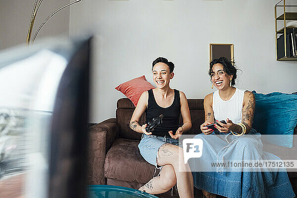 Cheerful lesbian couple watching TV on sofa