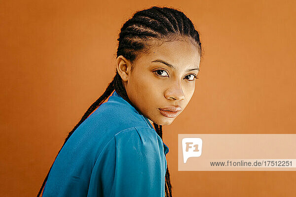 Young woman with braided hair staring by orange wall