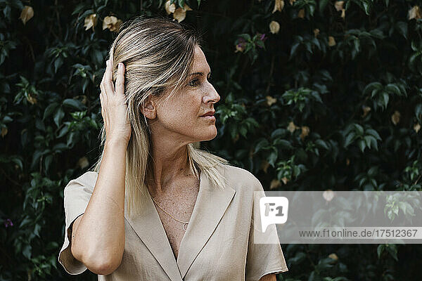 Close-up of thoughtful woman with hand in hair against plants