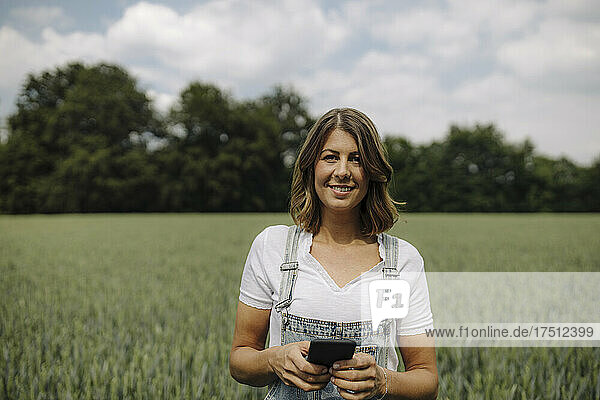 Young woman holding smartphone in a grain field in the countryside