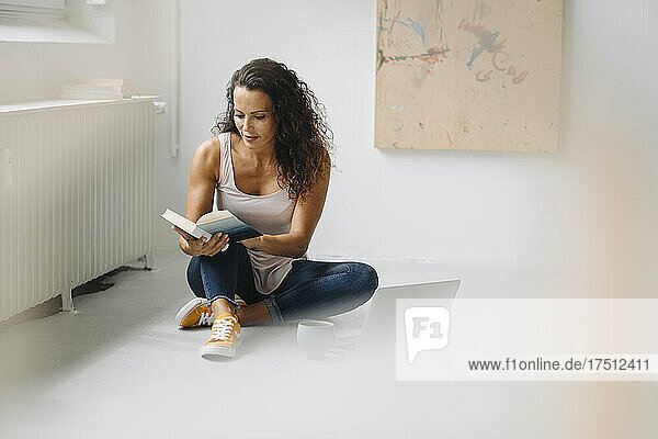 Mid adult woman reading book while sitting on floor at home