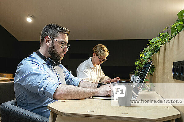 Businessman using laptop while working by female colleague at desk in illuminated coworking office