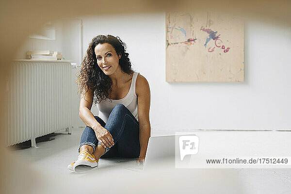 Smiling mid adult woman using laptop while sitting on floor in loft