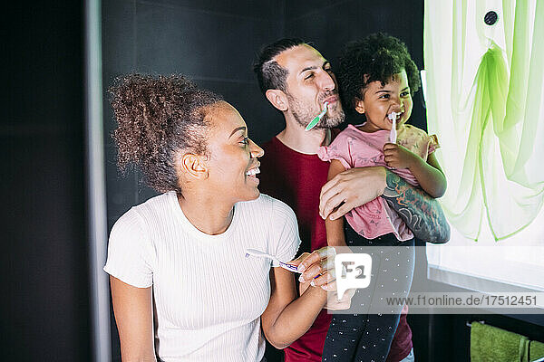 Happy parents with daughter brushing teeth in bathroom at home