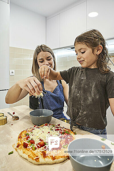 Mother and daughter throwing cheese on pizza dough in kitchen