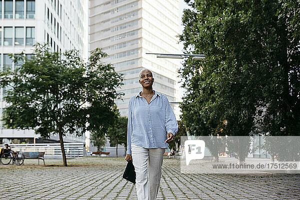 Smiling businesswoman with file walking in city