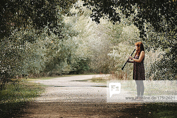 Young woman practicing clarinet while standing on footpath in forest