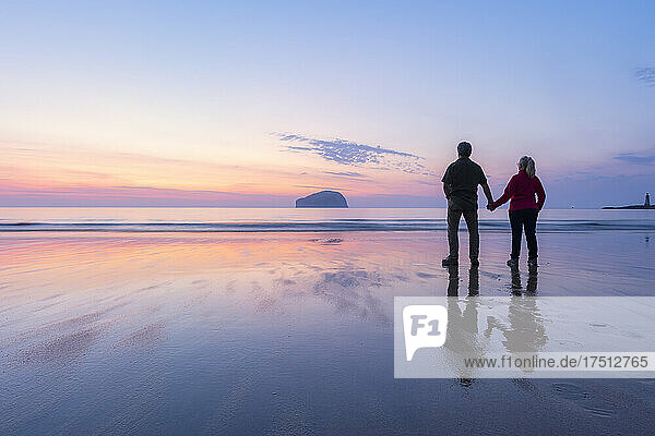 Couple looking at sea while standing on Seacliff Beach  North Berwick  Scotland during sunset