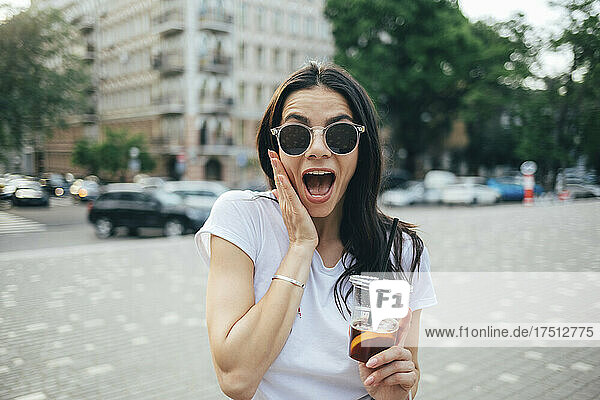 Cheerful woman wearing sunglasses with mouth open standing in city