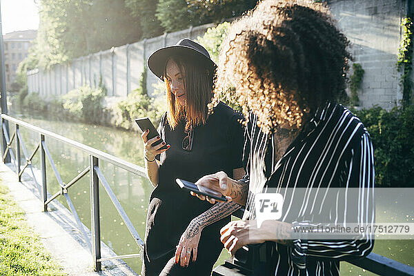 Couple using mobile phones while standing by railing against pond in park