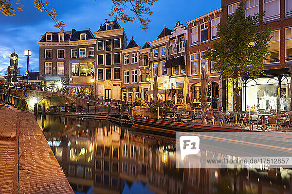 Netherlands  South Holland  Leiden  Sidewalk cafe and row of townhouses reflecting in Nieuwe Rijn canal at dusk