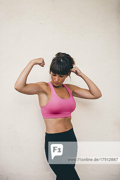 Fit woman flexing muscles while standing against wall