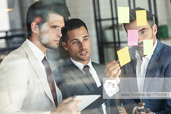 Businessman discussing with colleagues over adhesive notes stuck on glass