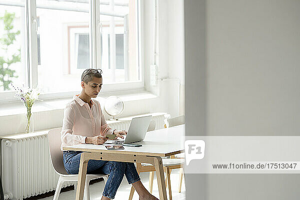 Geschäftsfrau hält Kreditkarte in der Hand und benutzt Laptop am Schreibtisch im Loft-Büro