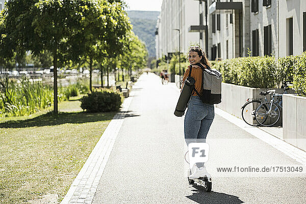 Smiling woman riding electric push scooter on road in city during sunny day