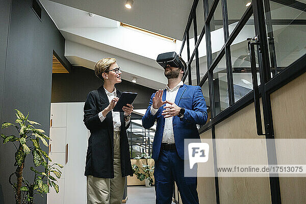 Businesswoman analyzing colleague using virtual simulation headset in creative office corridor