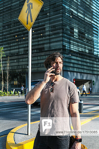 Man talking over smart phone looking away while standing on street in city