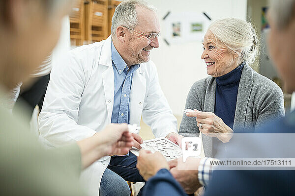 Doctor playing jigsaw puzzle with group of seniors in retirement home