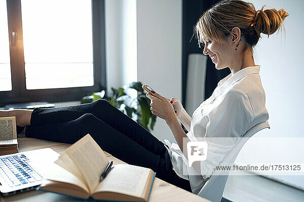 Smiling woman using phone at home office