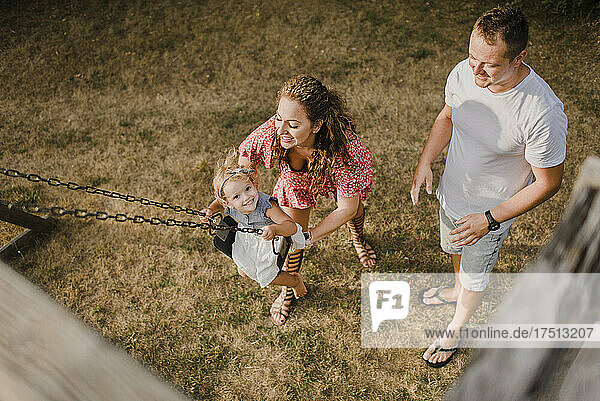 Happy girl with parents on a swing