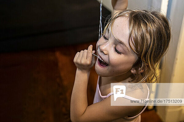 Close-up of cute girl using dental floss in bathroom at home