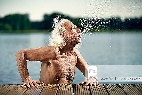Senior man with white hair leaning on jetty splashing with water