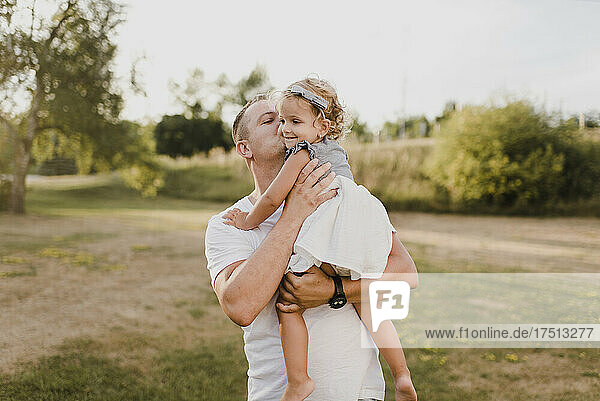 Father carrying and kissing little daughter on a meadow