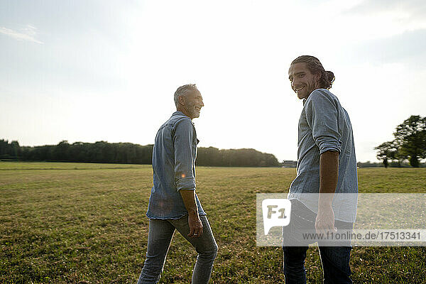 Happy father and adult son walking on a meadow in the countryside