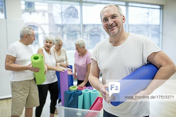 Happy mature man holding yoga mat after class