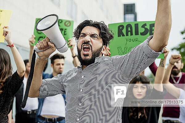 Mann hält Megaphon in der Hand und schreit mit Demonstranten auf der Straße
