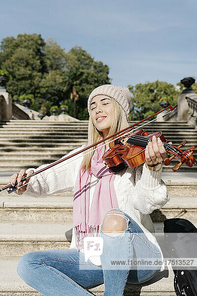 Blond young woman playing violin sitting on stairs