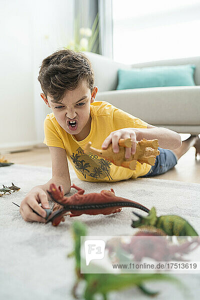 Boy playing with toy animals while lying on carpet in living room