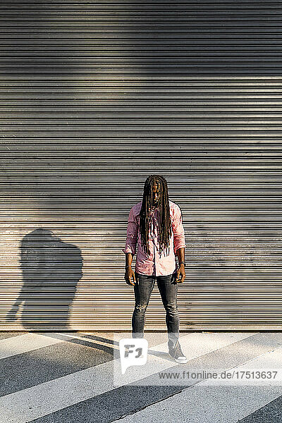 Afro young man with dreadlocks standing on street against wall