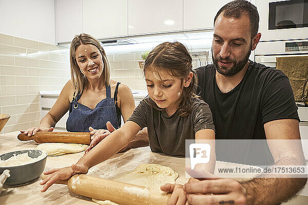 Family kneading pizza dough with rolling pins on table in kitchen