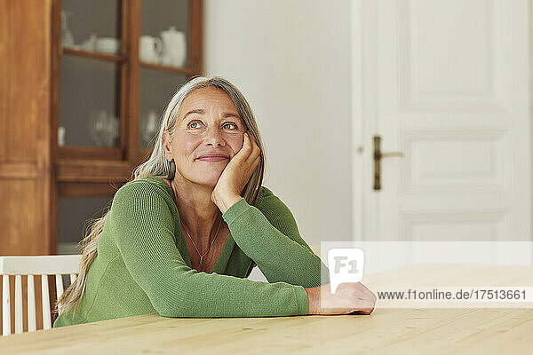 Smiling woman day dreaming while sitting by table at home