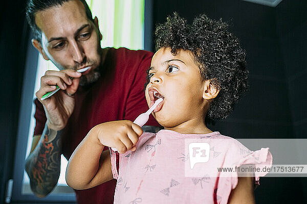 Close-up of daughter with father brushing teeth in bathroom at home