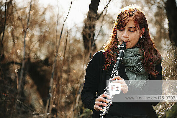 Beautiful redhead woman practicing clarinet in forest