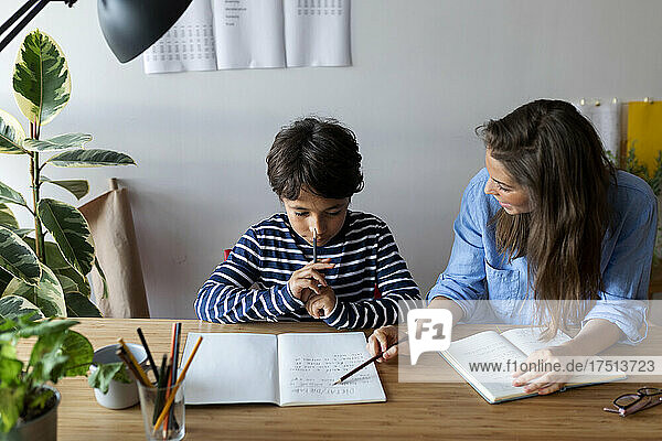 Female tutor explaining to boy through book on table at home