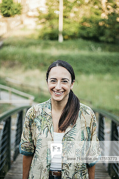Smiling woman standing over footbridge in public park