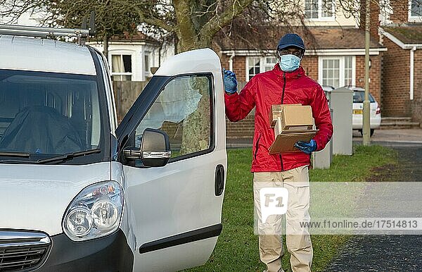 Männlicher Kurier  der während der Covid-19-Epidemie Pakete und Päckchen ausliefert und dabei Handschuhe und einen Mundschutz trägt  Hampshire  England  Vereinigtes Königreich.